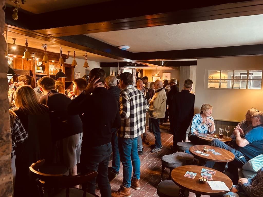 The busy bar at The Eight Bells, Bolney — brass bells above the counter